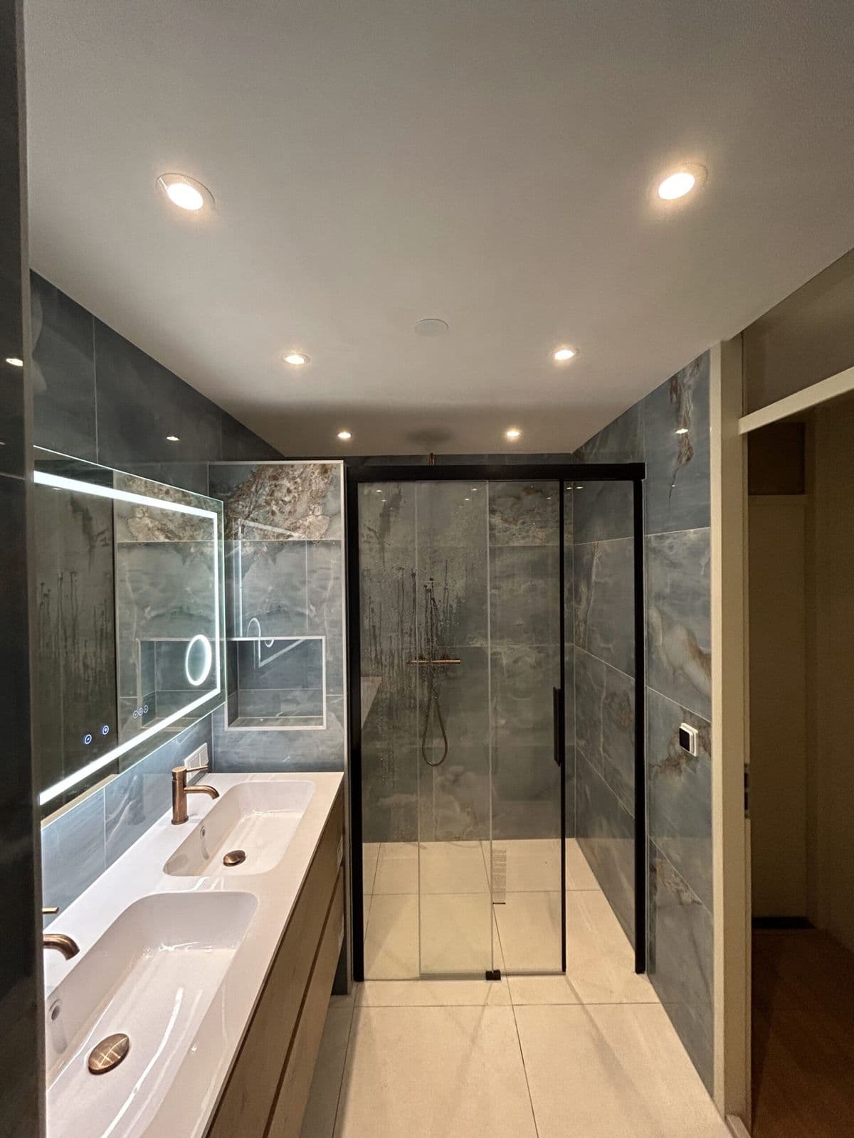 Badkamer met led-spiegel, houten meubel en douche met schuifdeur